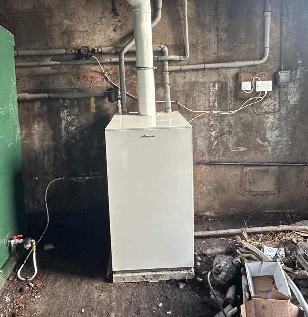 White boiler unit with pipes against a stained wall in a cluttered utility area
