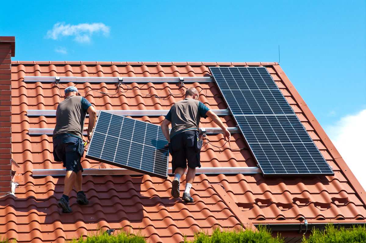 Two installers fitting solar panels on a tiled roof